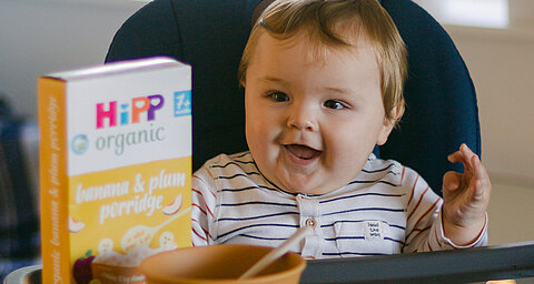 Baby sitting in highchair enjoying a HiPP porridge