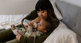 Mum bottle feeding baby on sofa