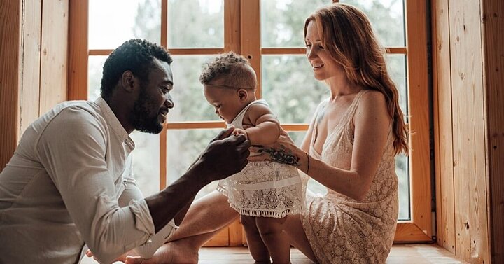 Parents sat playing in window bay with baby