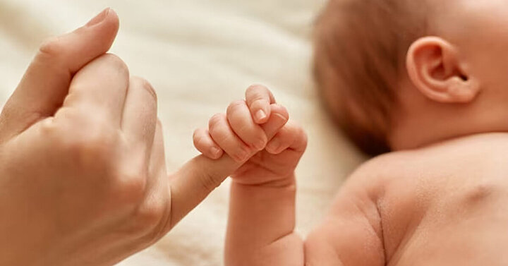 Newborn baby holding mother's finger