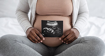 Pregnant woman holding ultrasound scan image against stomach