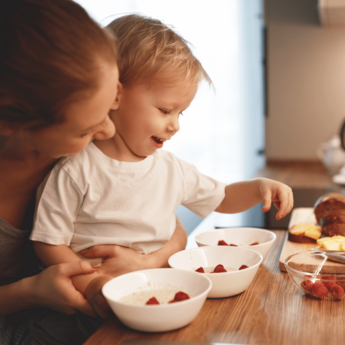 Mum and baby making up bowls of porridge topped with raspberries