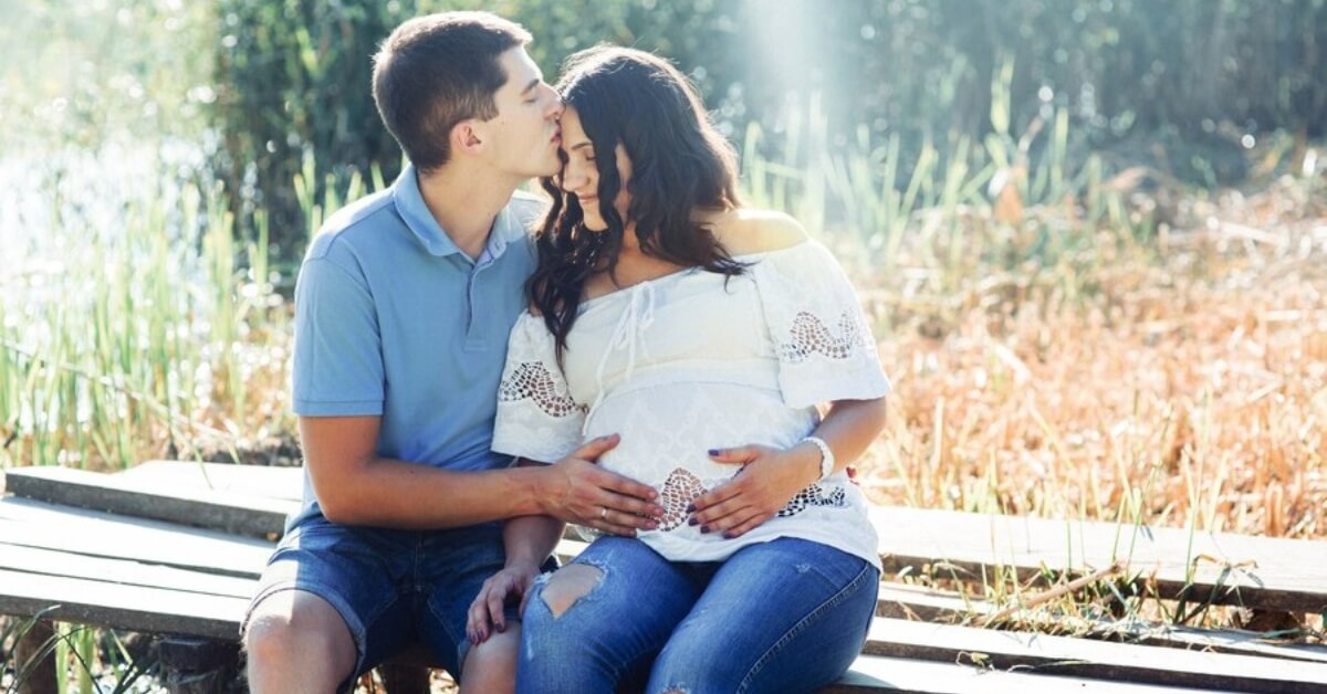 Expecting parents sat on bench in field