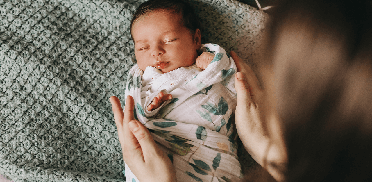 Mum swaddling baby in leaf print blanket