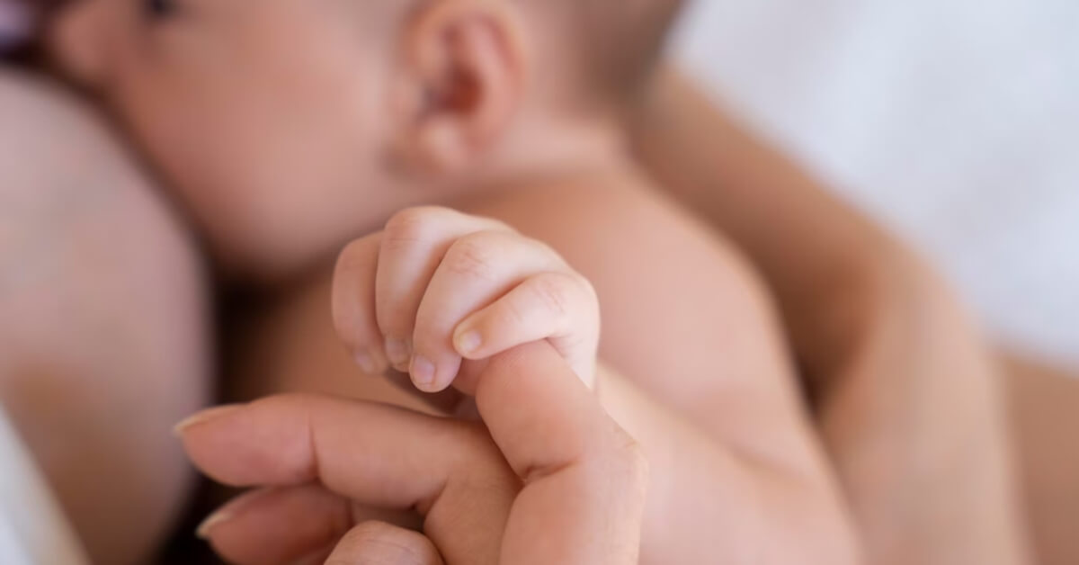Baby holding mum's finger whilst breastfeeding