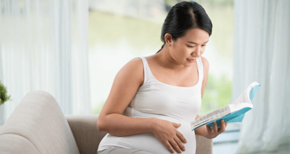 Woman reading a book while holding her bump